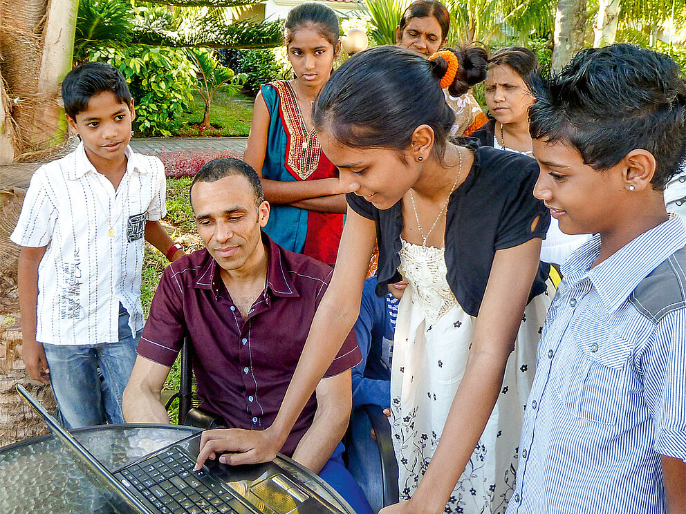 Kofi Yakpo mit Jugendlichen an einem Laptop im Freien